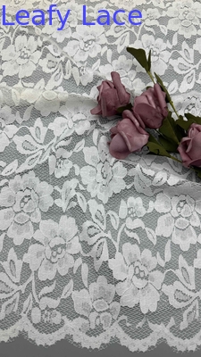 Tessuto di pizzo a tutta larghezza in bianco, decorato con delicati disegni floreali e bordi ricci lussuosamente