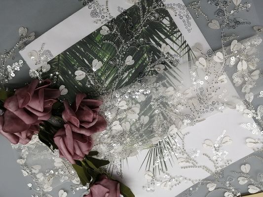 Lo zecchino bianco dell'indumento femminile merletta il tessuto in rilievo del ricamo